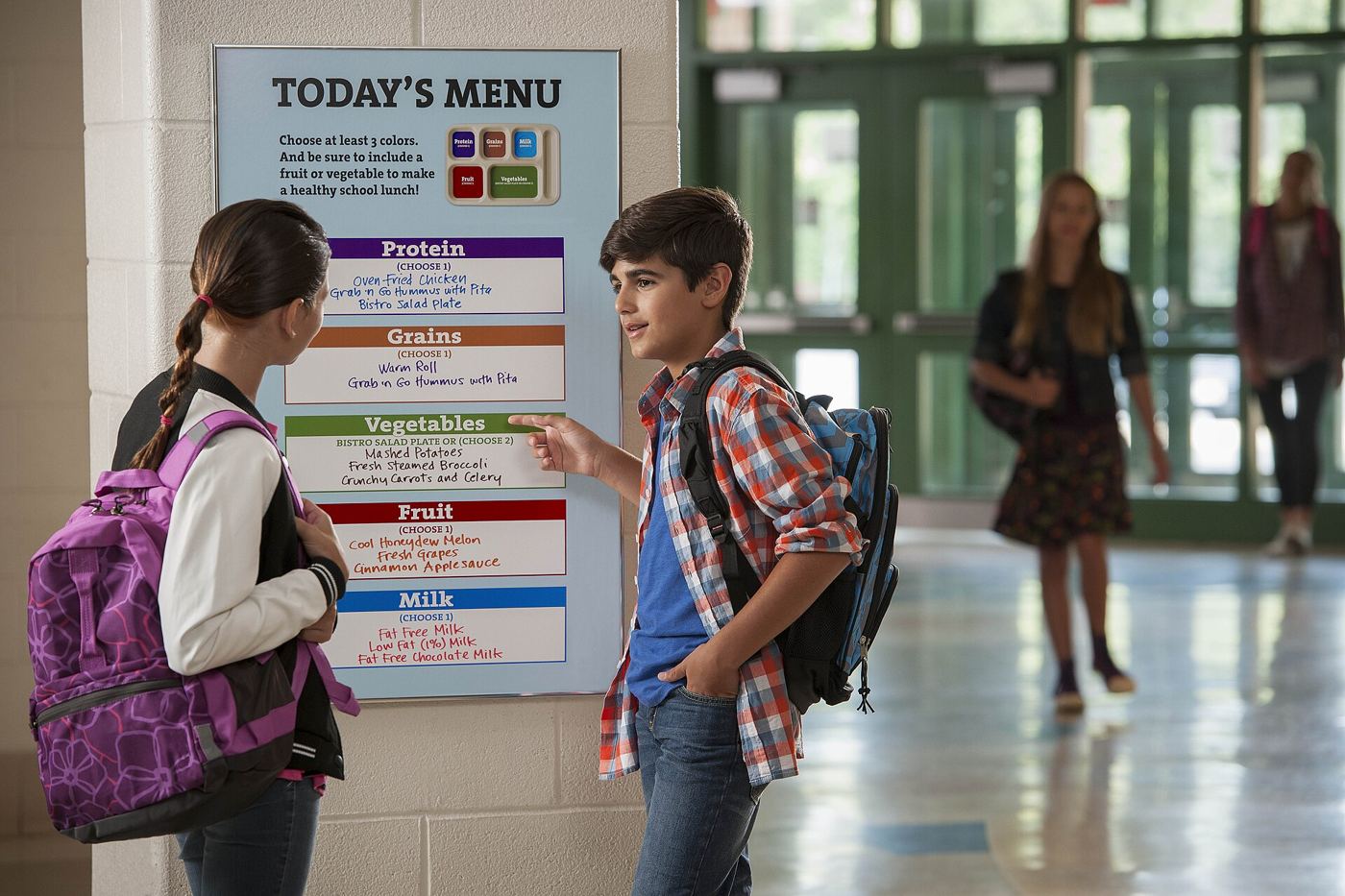 Children eat a balanced lunch together at tables in a bright school cafeteria.